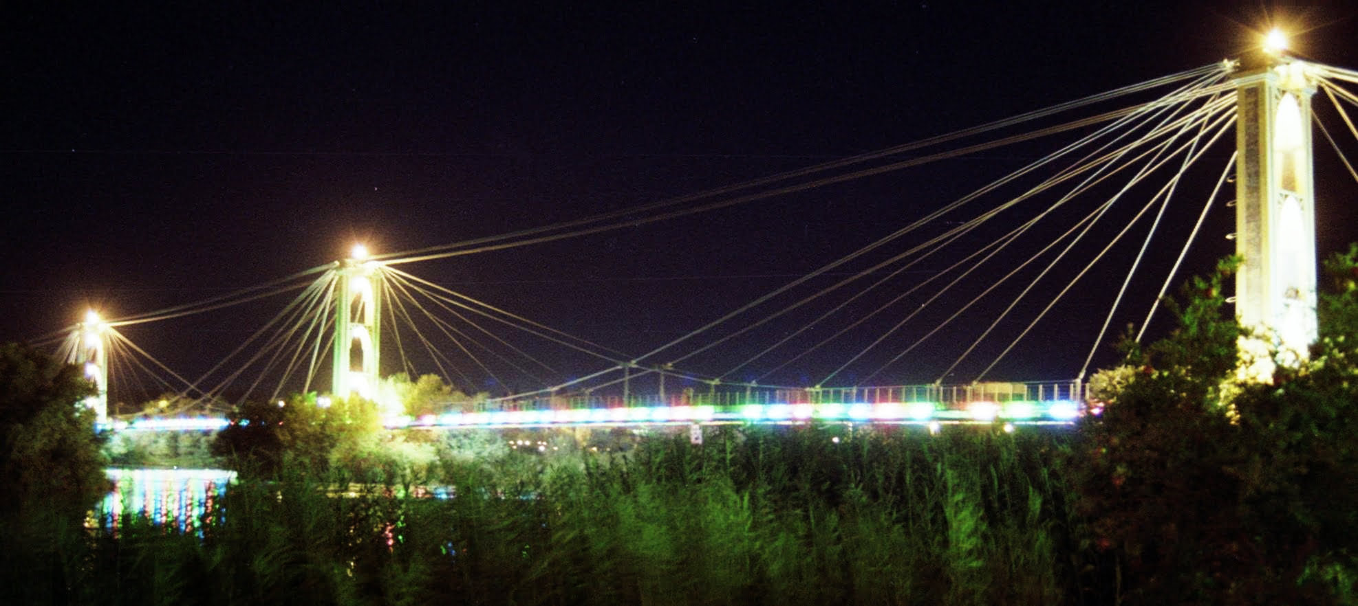 Deir ez-Zor suspension bridge at night in October 2010, by Fulvio Spada, used under CC BY-SA 2.0. / Contrast adjustment from original. The suspension bridge, which was built in the 1920s and spanned the Euphrates River, was destroyed in May 2013.